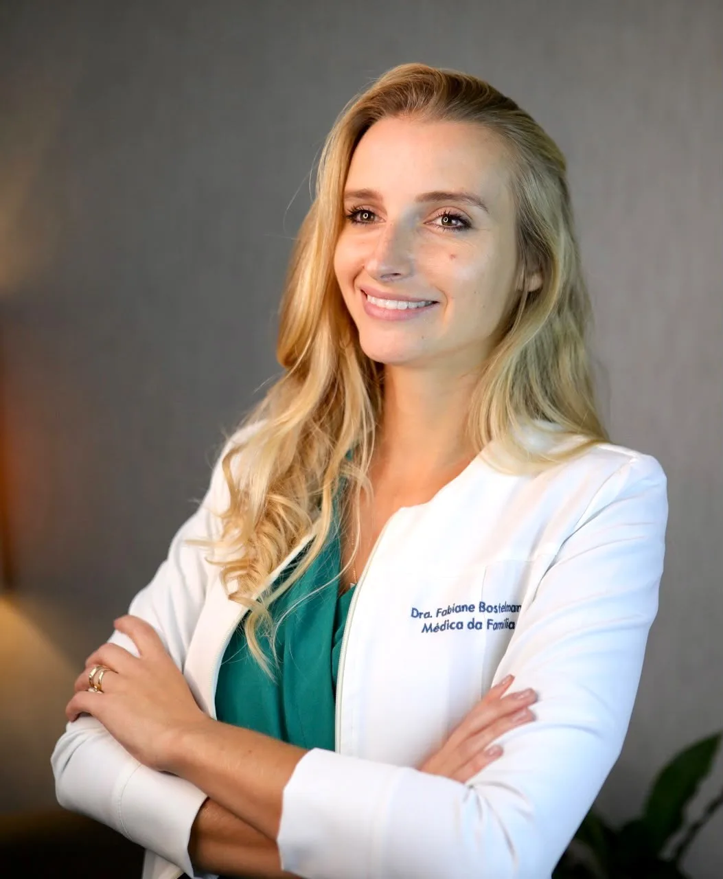 Dra. Fabiane Bostelmann de jaleco branco, sorrindo, de braços cruzados